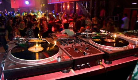 Turntables in focus at a bustling nightclub.