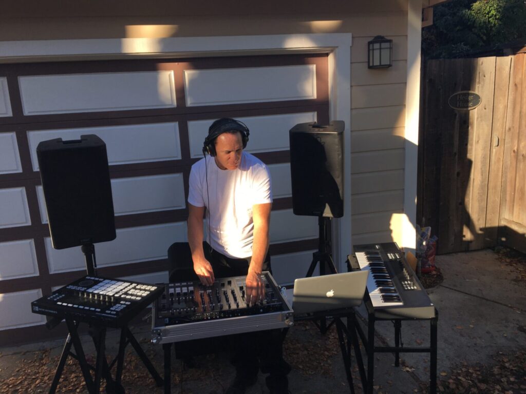 Man operating a dj mixing console outdoors in front of a garage.