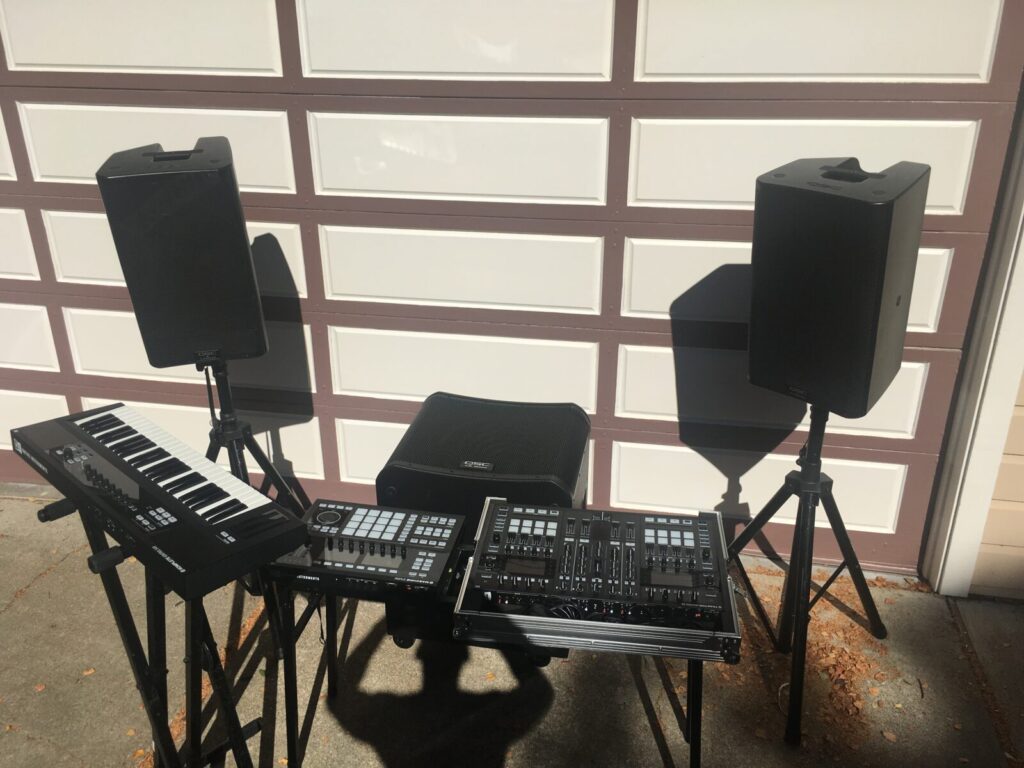 Music equipment set up outside, featuring keyboards and speakers on stands in front of a garage door.