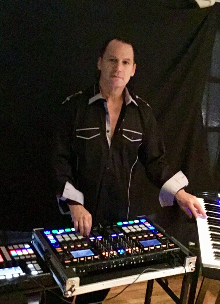 Man playing electronic keyboard and operating a sound mixer at a music event.