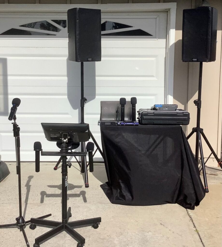 A portable pa system setup with two speakers on stands, a mixer on a covered table, and two microphones on stands.
